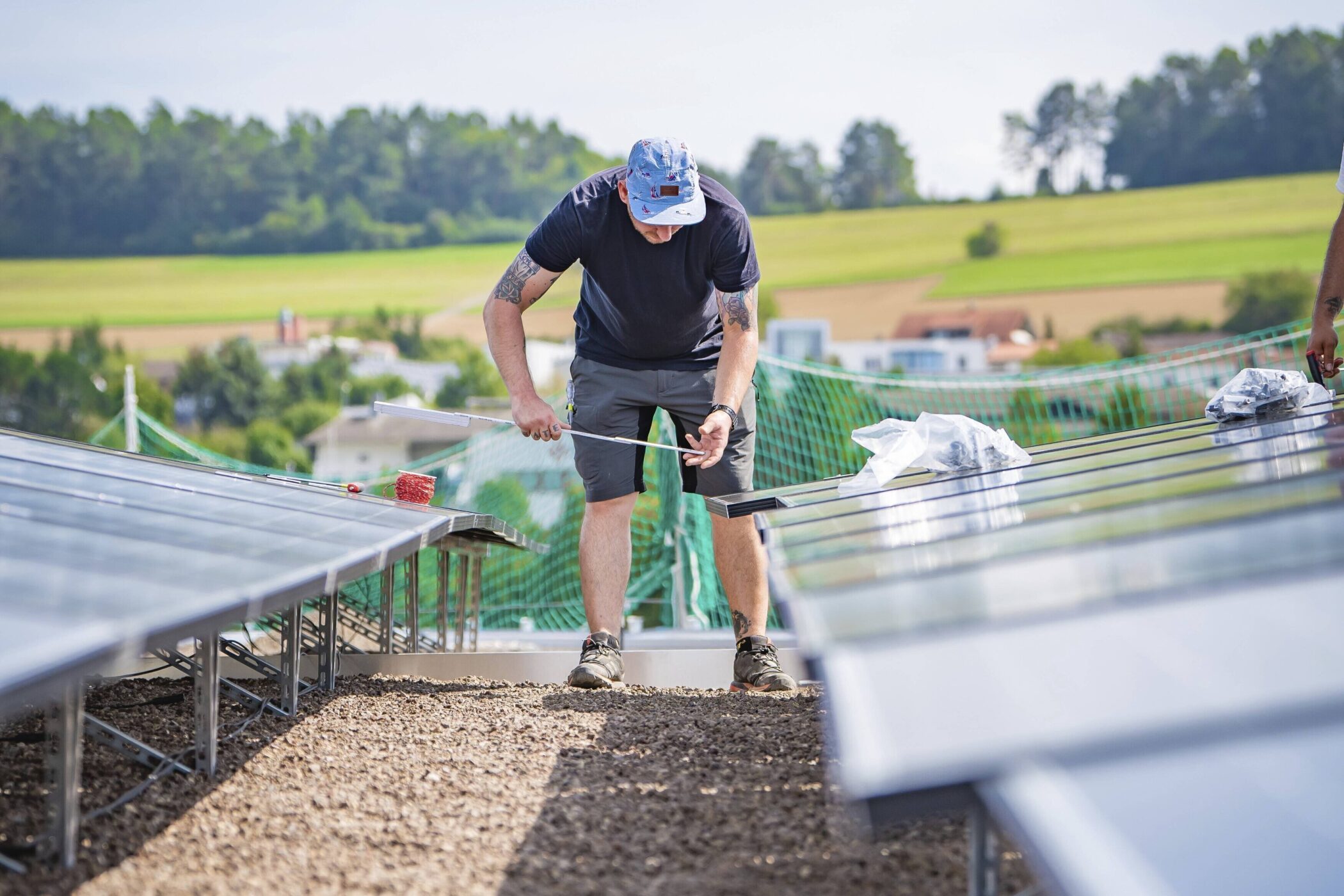 Person steht zwischen Solarpanelen auf einem Dach, arbeitet mit Werkzeug.