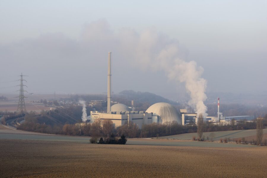 Kraftwerk mit Rauch, zwei große Kuppeln, Strommast links, winterliche Landschaft.