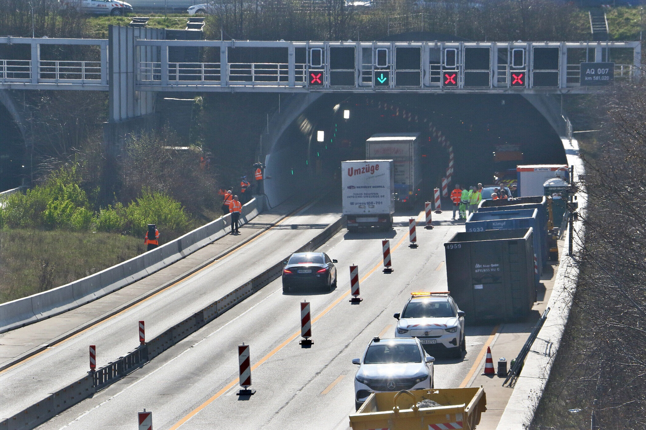 Tunnelbaustelle mit mehreren Fahrzeugen und Menschen in Warnwesten. Verkehrsabsperrung.