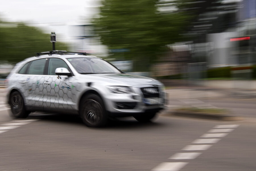 Silbernes Auto mit hexagonalem Muster fährt durch eine Stadtstraße.