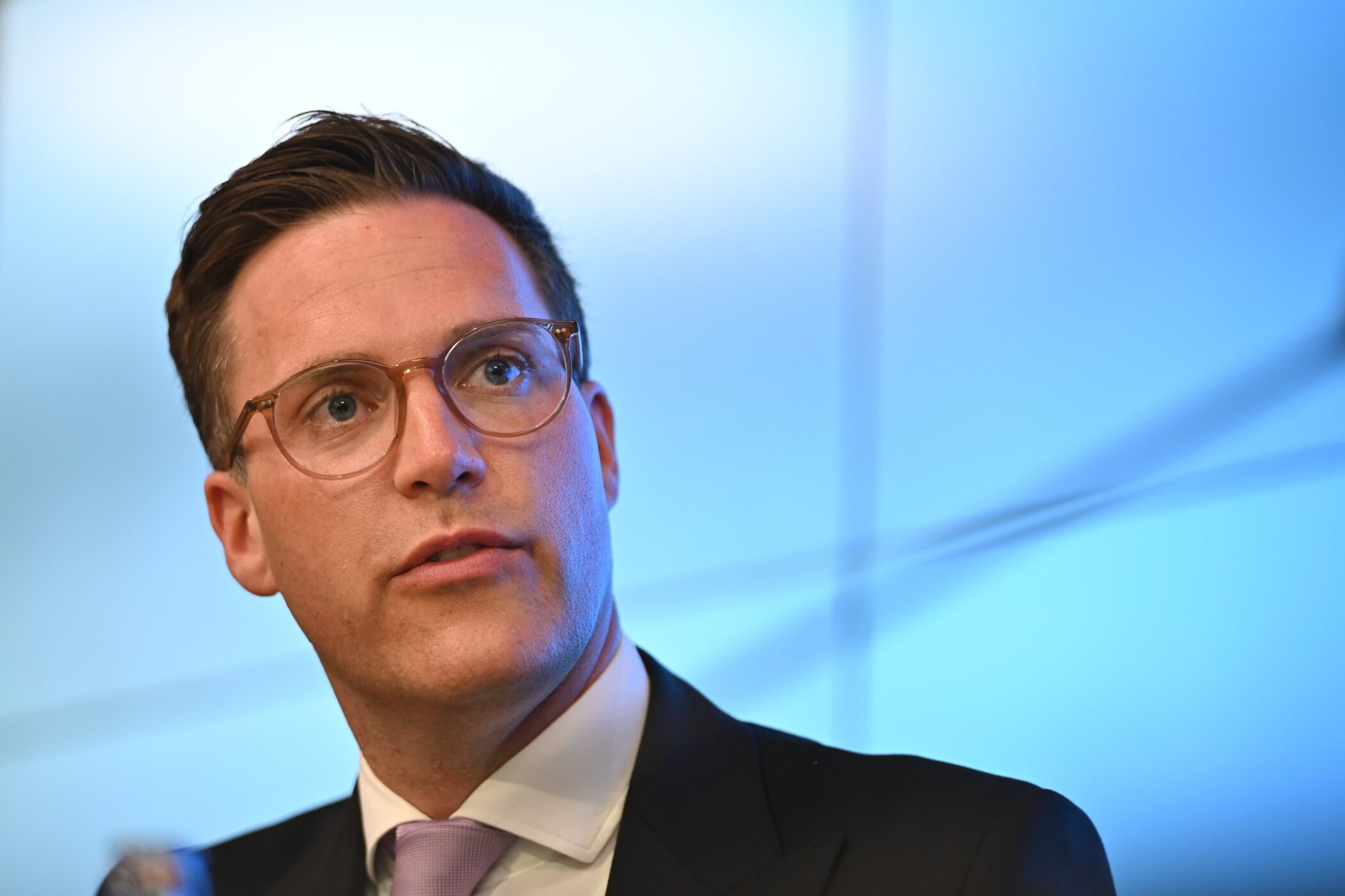 Eine Person mit Brille spricht, Hintergrund blau.