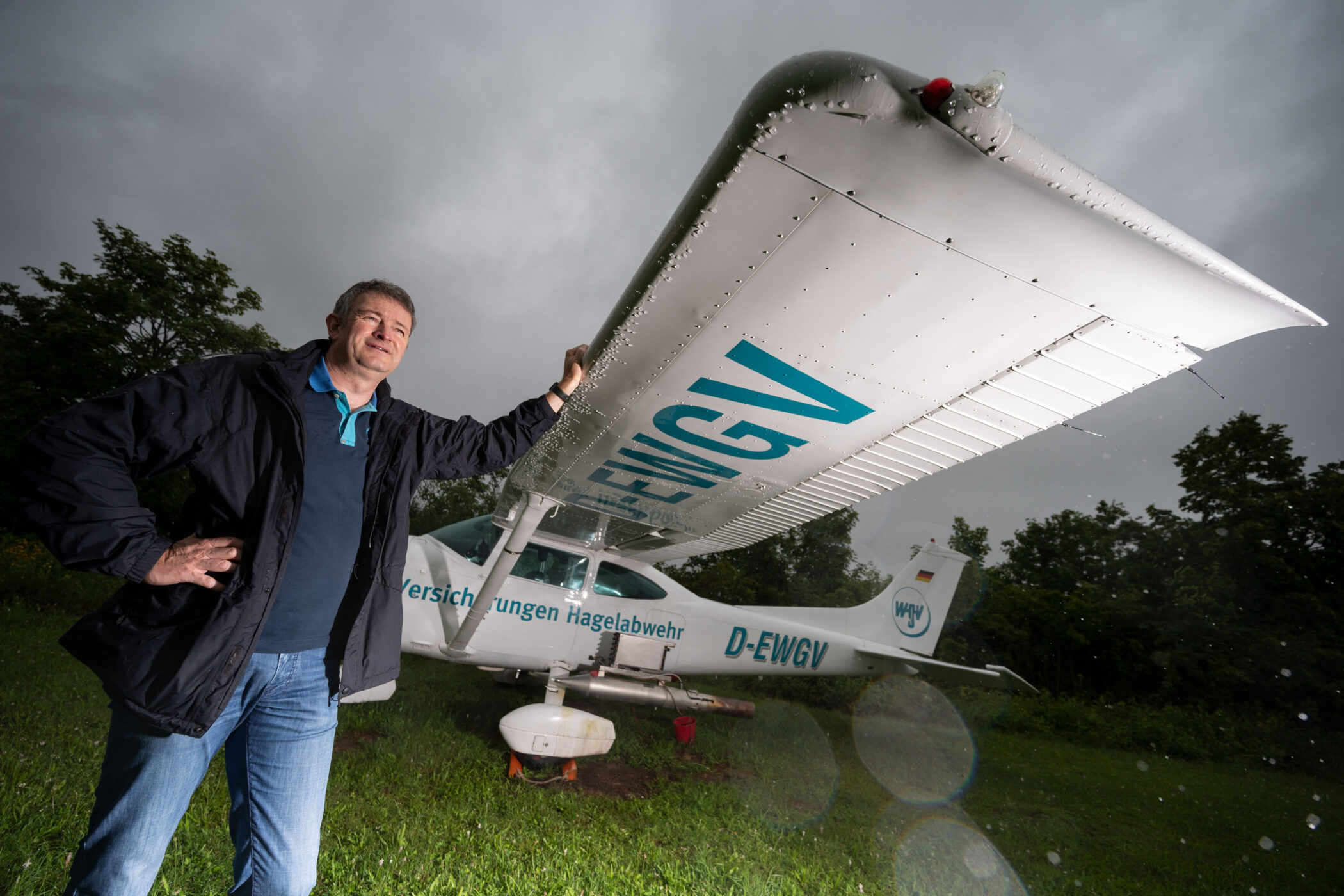Mann lehnt an Tragfläche eines kleinen Flugzeugs auf einer Wiese.