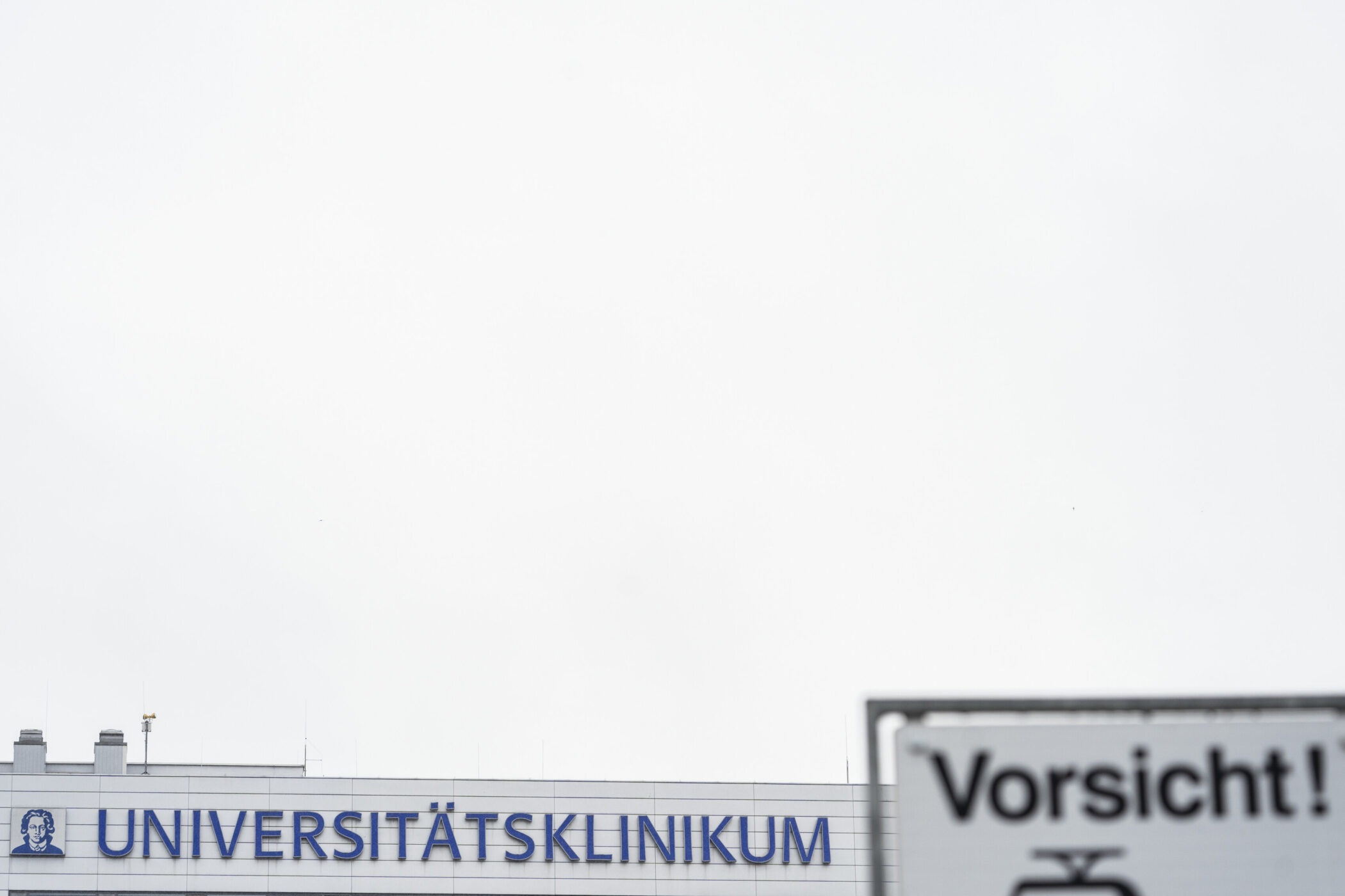 Gebäude mit Aufschrift "UNIVERSITÄTSKLINIKUM", Schild mit "Vorsicht!" davor.