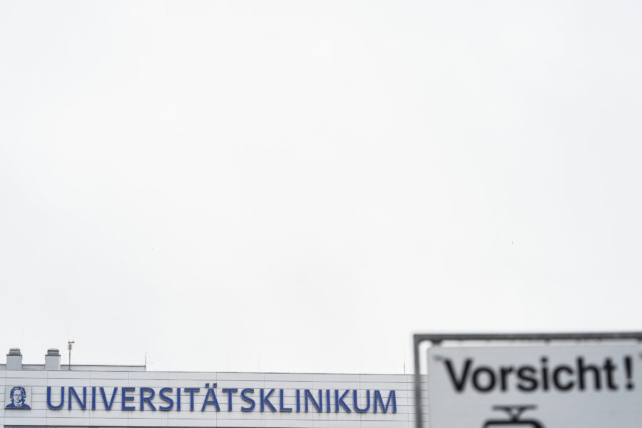 Gebäude mit Aufschrift "UNIVERSITÄTSKLINIKUM", Schild mit "Vorsicht!" davor.