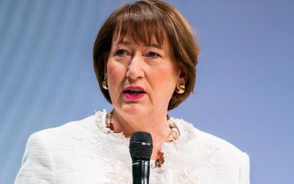 Eine Person spricht in ein Mikrofon vor neutralem Hintergrund.