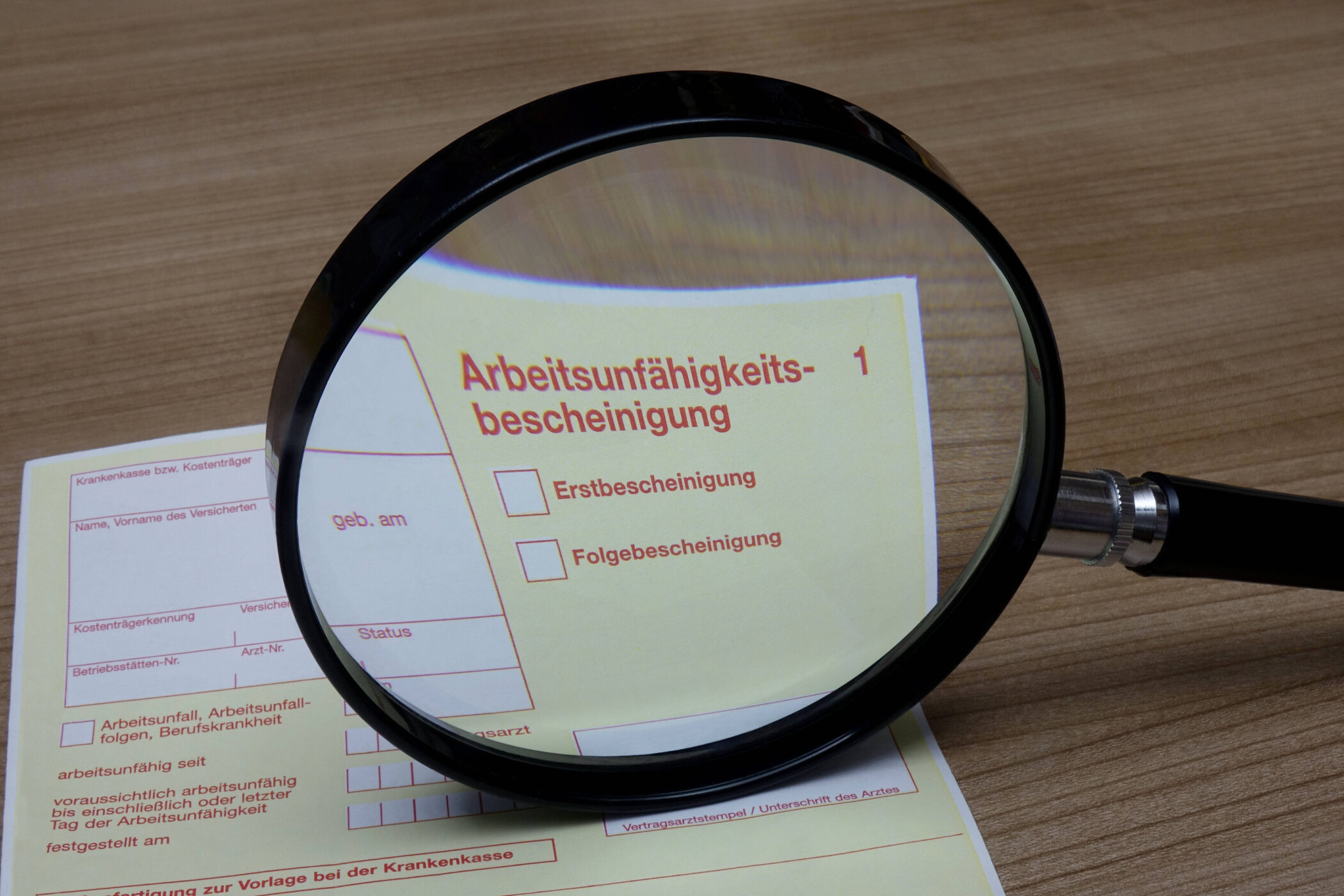 Vergrößerte Arbeitsunfähigkeitsbescheinigung durch Lupe auf Holztisch.