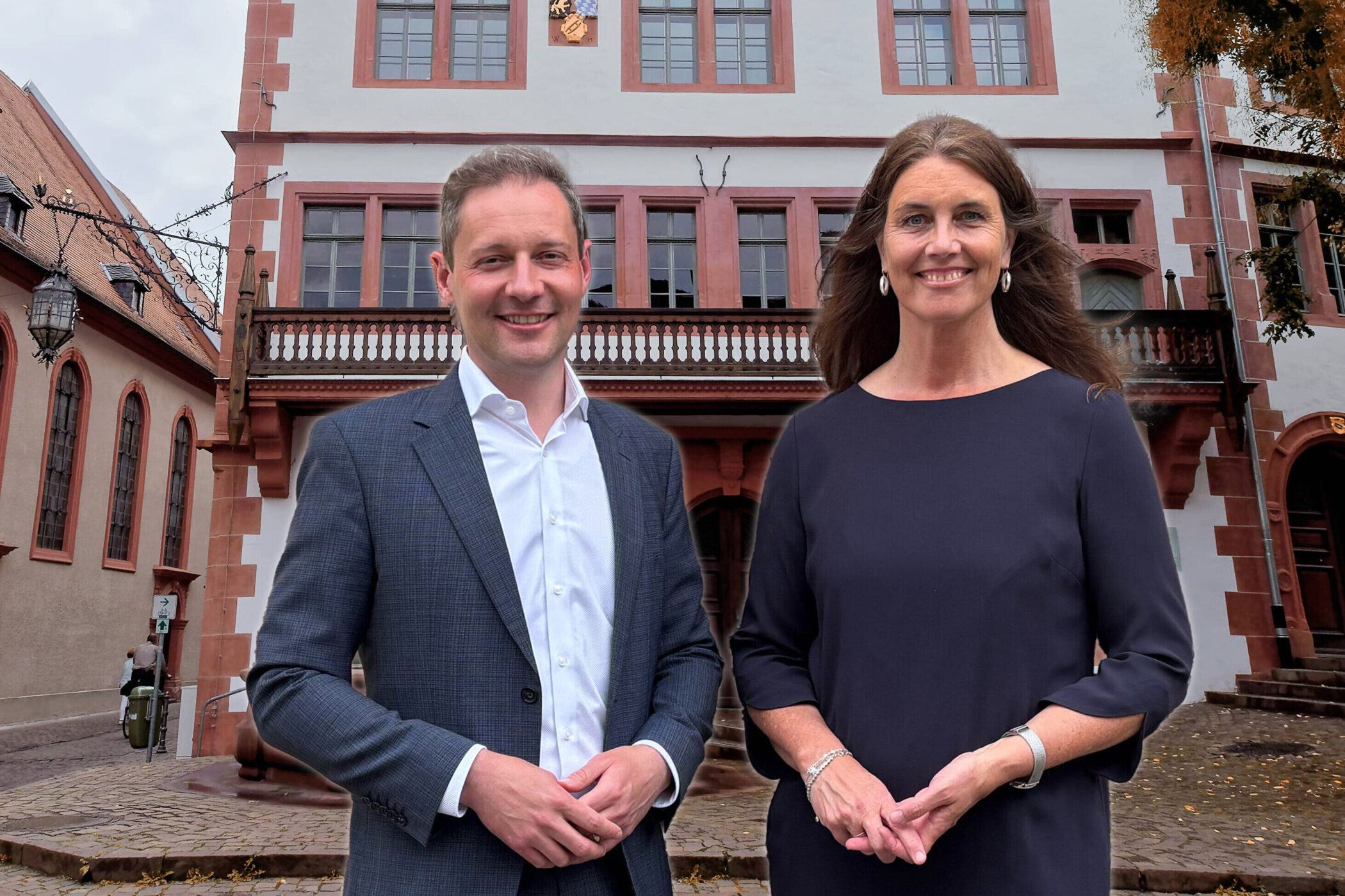 Zwei Personen stehen vor einem historischen Gebäude mit roten Fenstereinfassungen.