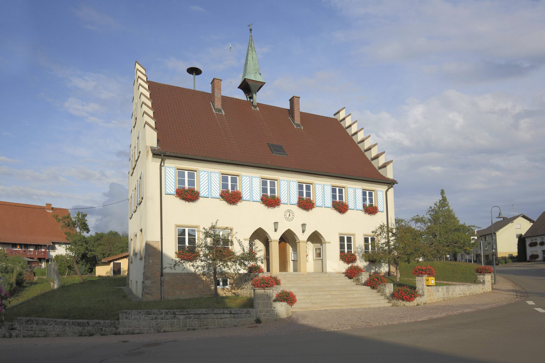 Zweistöckiges Gebäude mit rotem Dach und blauen Fensterläden, Blumenkästen.