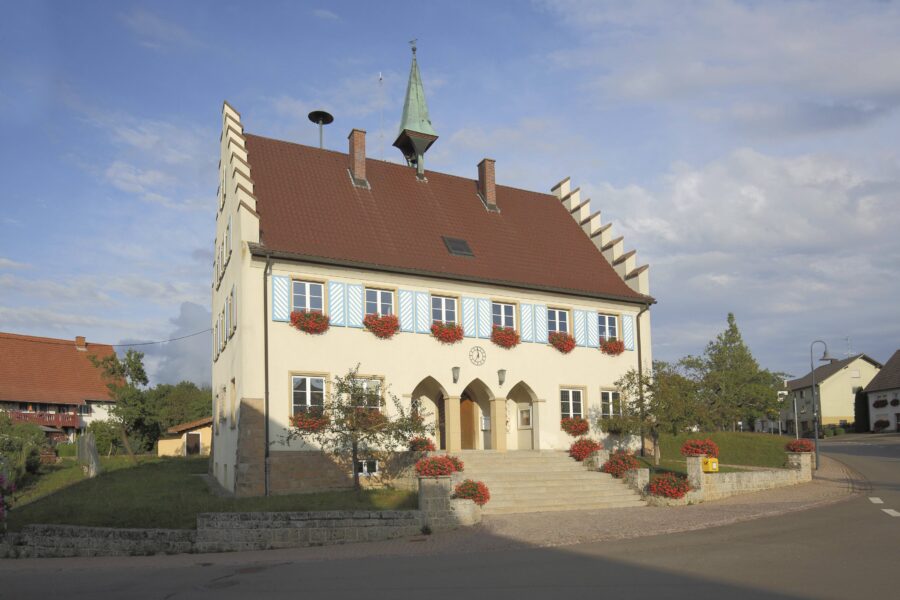 Zweistöckiges Gebäude mit rotem Dach und blauen Fensterläden, Blumenkästen.