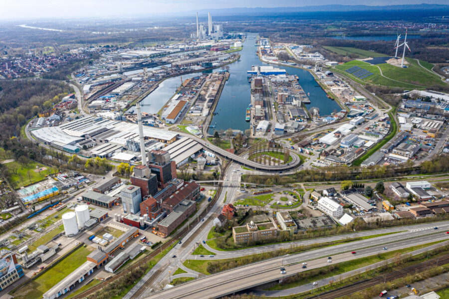 Luftaufnahme eines Industriegebiets mit Fluss, Straßen und Windkraftanlage.