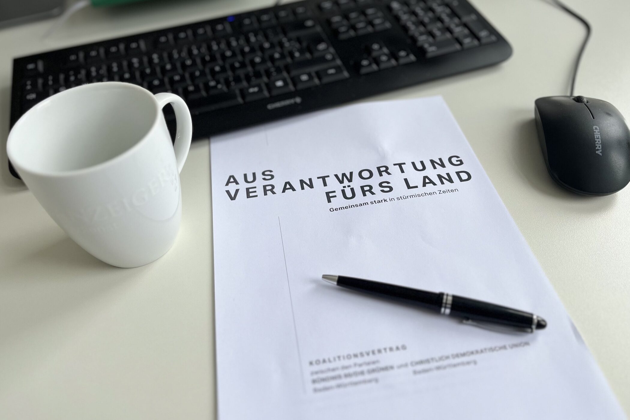 Computertastatur, Maus, Tasse, Dokument mit Stift auf einem Tisch.