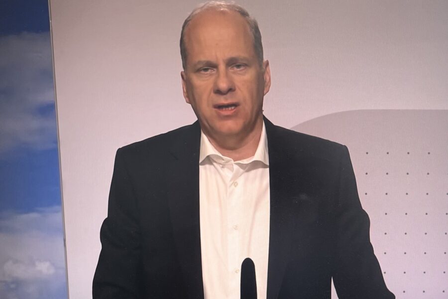 Mann in schwarzem Anzug und weißem Hemd spricht vor Mikrofon.