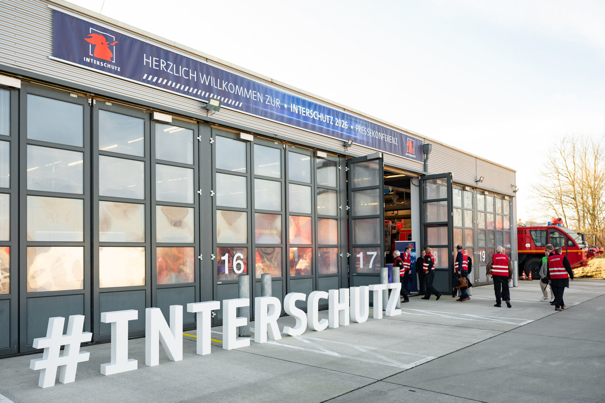 Gebäude mit Banner „Interschutz 2026“, Feuerwehrleute betreten die Halle.