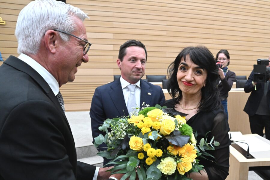 Drei Personen, eine hält einen Blumenstrauß. Fotografen im Hintergrund.