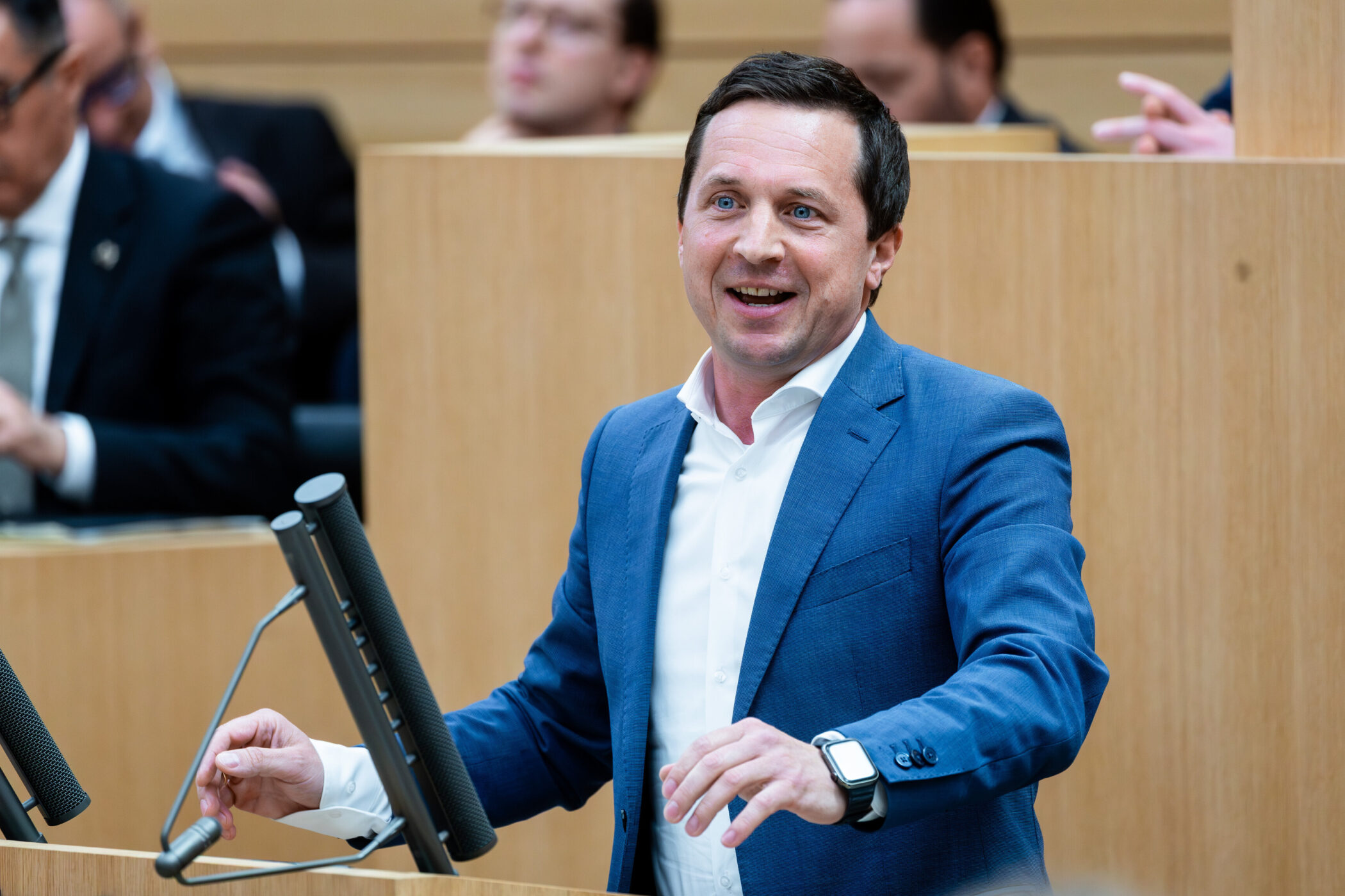 Ein Mann spricht an einem Rednerpult, mehrere hören zu.