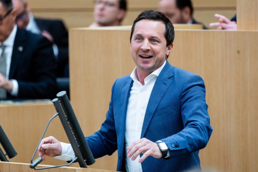 Ein Mann spricht an einem Rednerpult, mehrere hören zu.