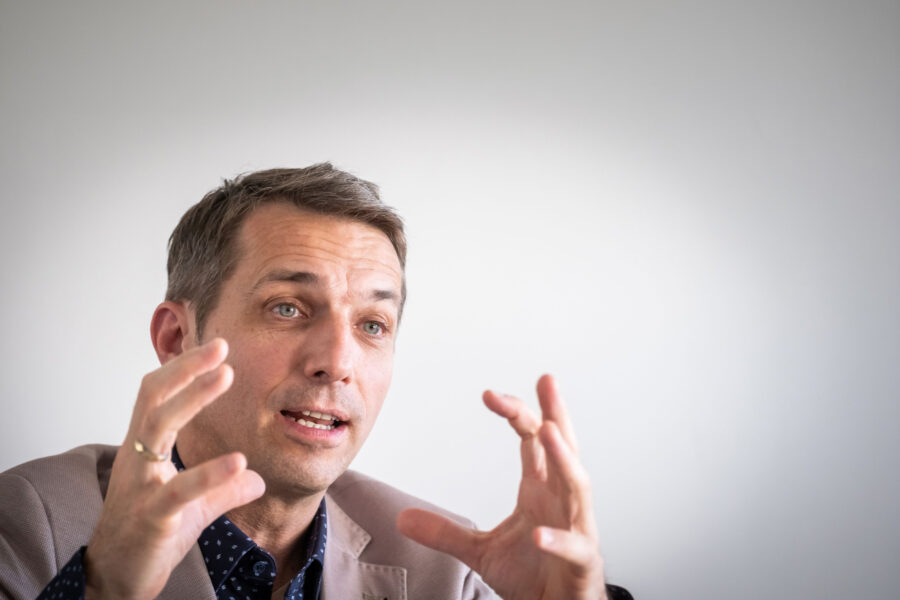 Ein Mann gestikuliert mit beiden Händen vor einem hellen Hintergrund.