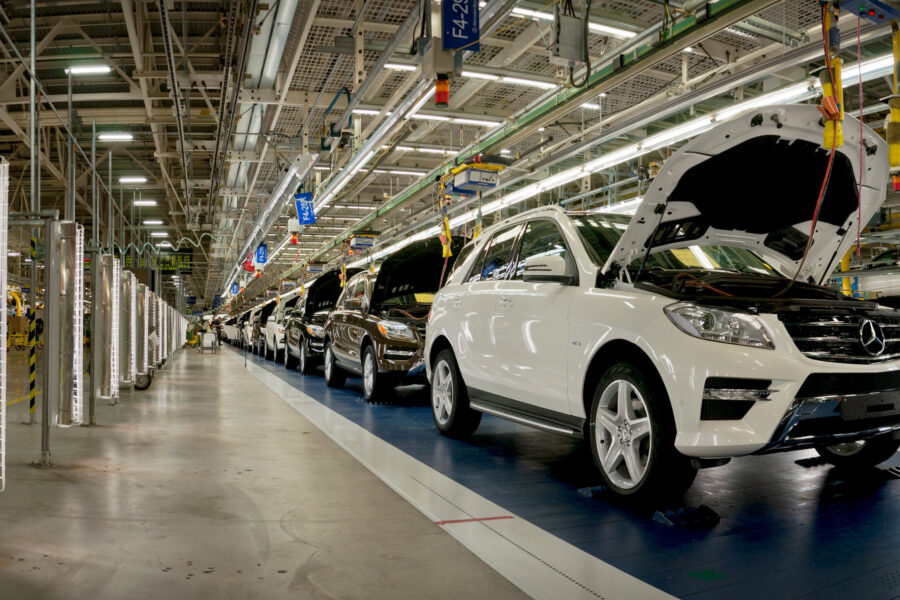 Reihe von SUVs mit offenen Motorhauben auf einem Fließband in einer Fabrikhalle.