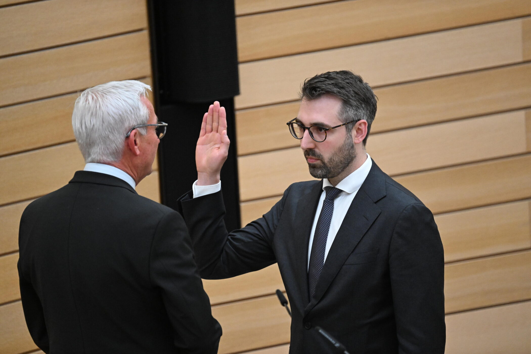 Zwei Männer in Anzügen, einer hebt die Hand.