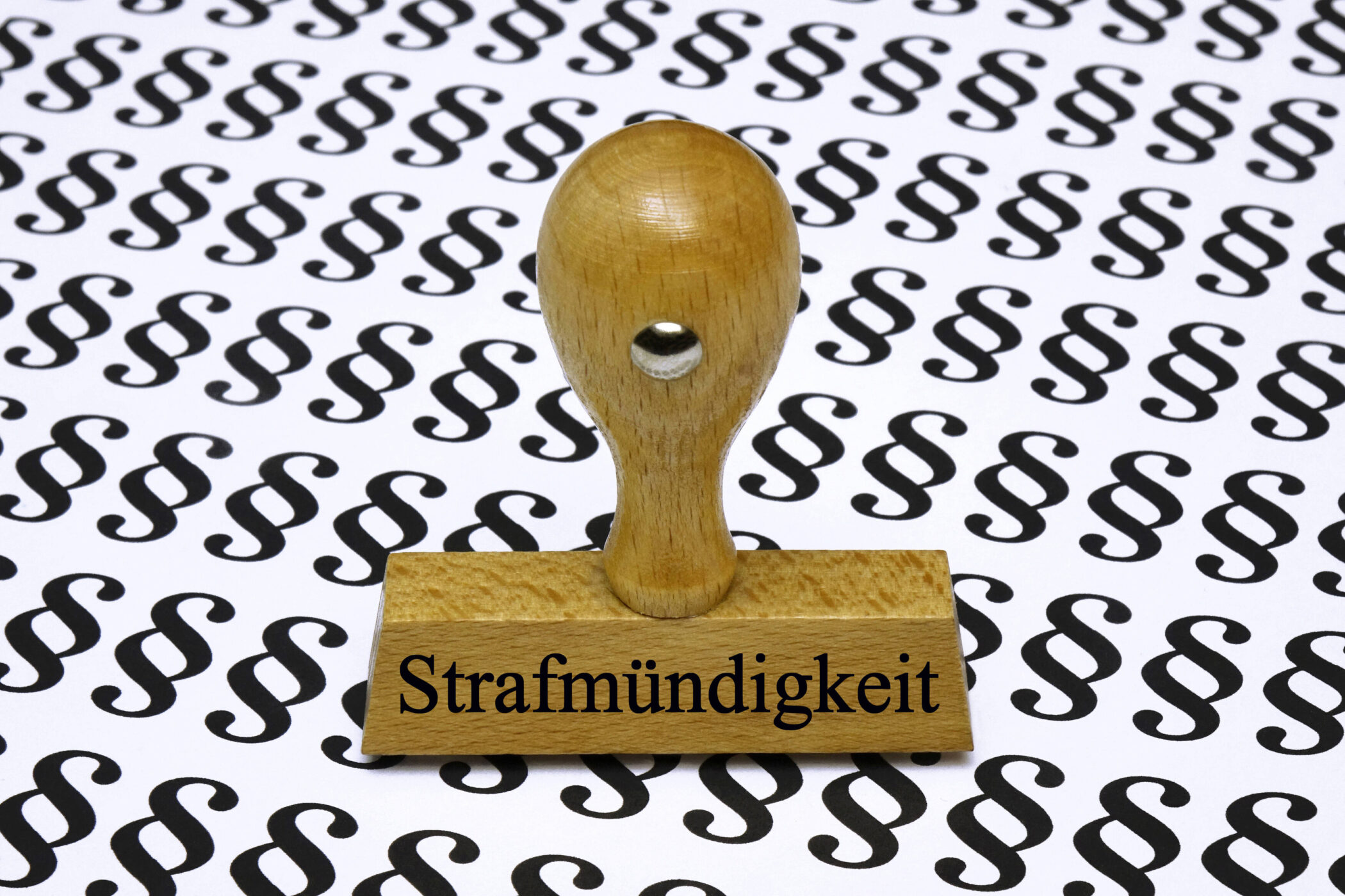 Holzstempel mit Aufschrift "Strafmündigkeit" vor §-Symbol-Hintergrund.