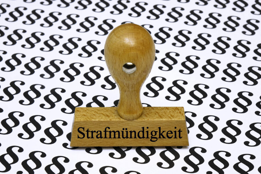 Holzstempel mit Aufschrift "Strafmündigkeit" vor §-Symbol-Hintergrund.