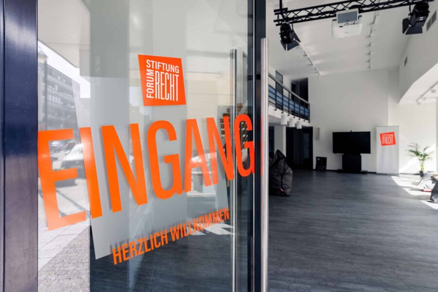 Glastür mit Schriftzug "Eingang" und "Herzlich Willkommen" in orange.