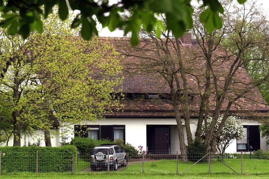 Weißes Haus mit braunem Ziegeldach, Bäume und ein Auto im Vorgarten.