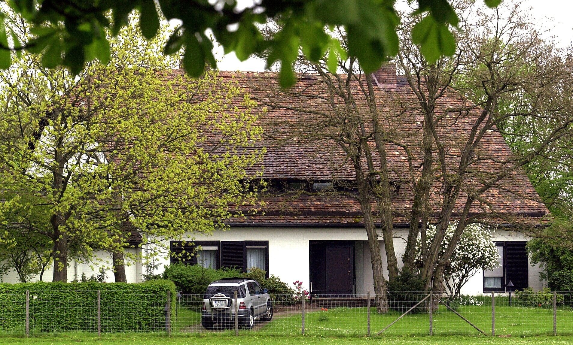 Weißes Haus mit braunem Ziegeldach, Bäume und ein Auto im Vorgarten.