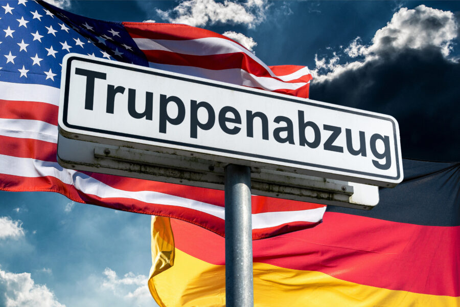Straßenschild mit „Truppenabzug“, USA- und Deutschlandflagge im Hintergrund.
