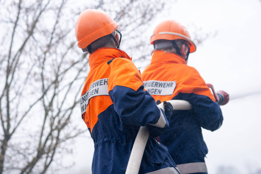 Zwei Personen in Feuerwehrkleidung halten einen Schlauch.