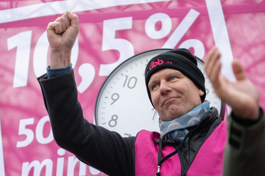 Mann mit erhobener Faust, pinker Hintergrund mit 10,5 %, große Uhr im Hintergrund.