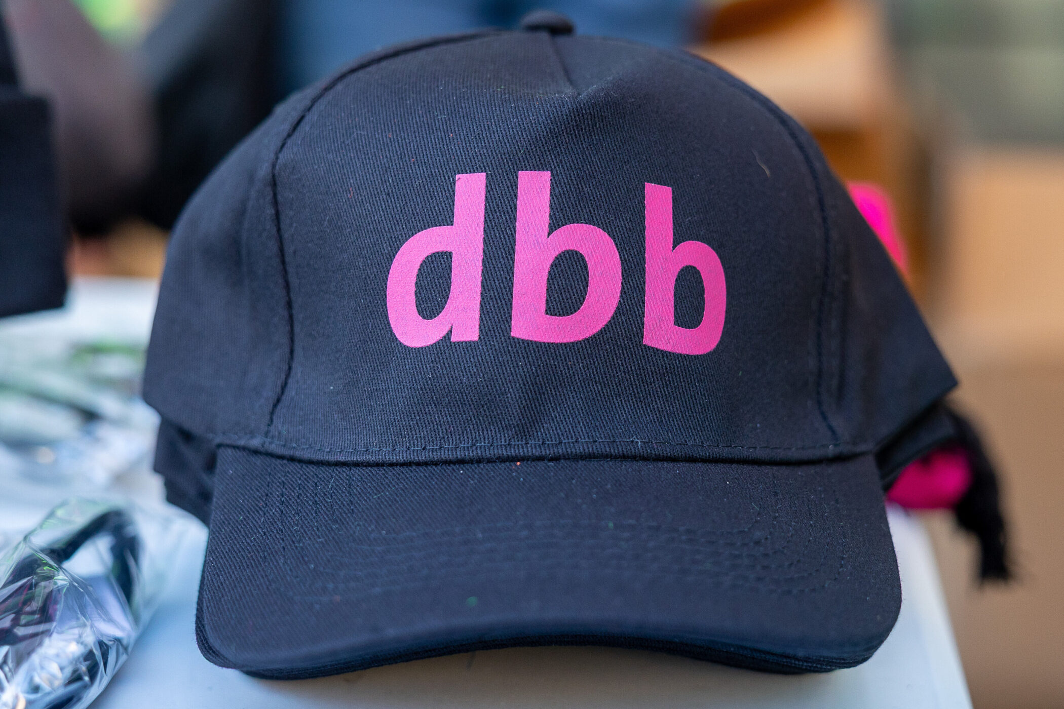 Schwarze Kappe mit rosa Schrift "dbb" auf einem Tisch.