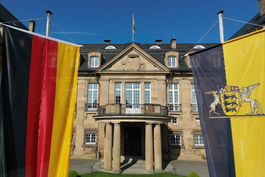 Gebäude mit Säulen, zwei große Flaggen, blauer Himmel.