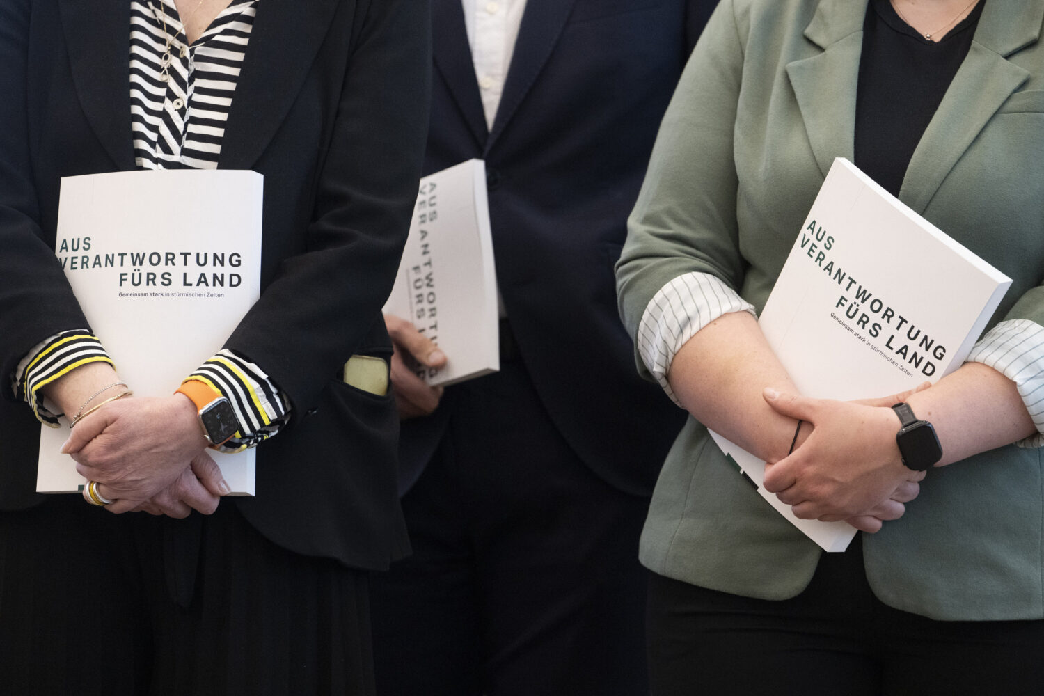 Drei Personen halten Mappen mit der Aufschrift „AUS VERANTWORTUNG FÜRS LAND“.