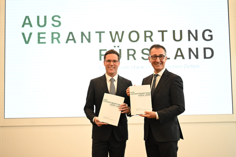 Zwei Männer in Anzügen halten Bücher mit „AUS VERANTWORTUNG FÜRS LAND“.