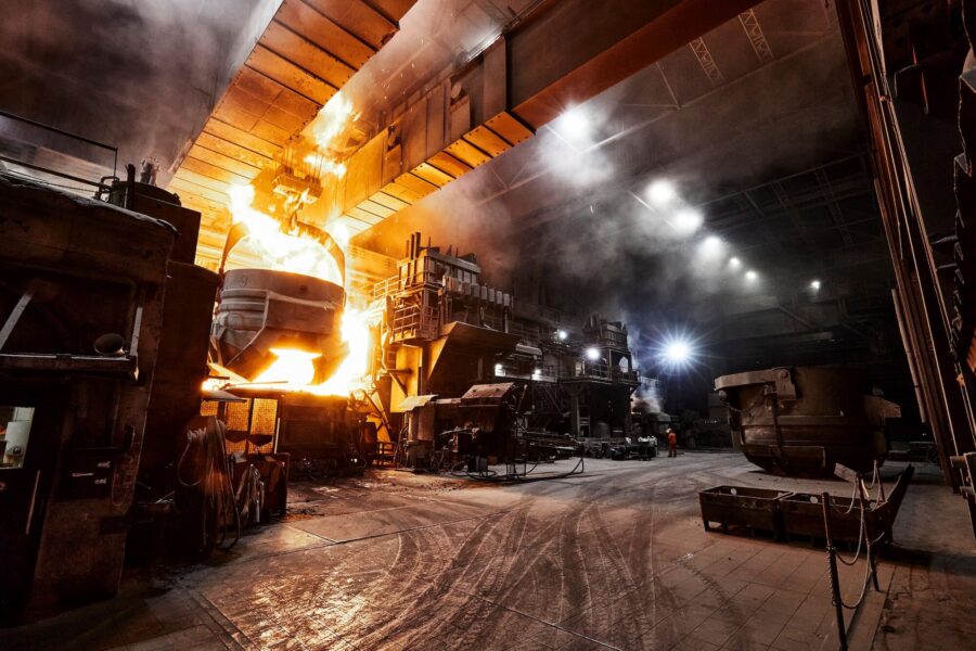 Fabrikhalle mit gleißender Flamme aus einem Kessel, Maschinen im Hintergrund.