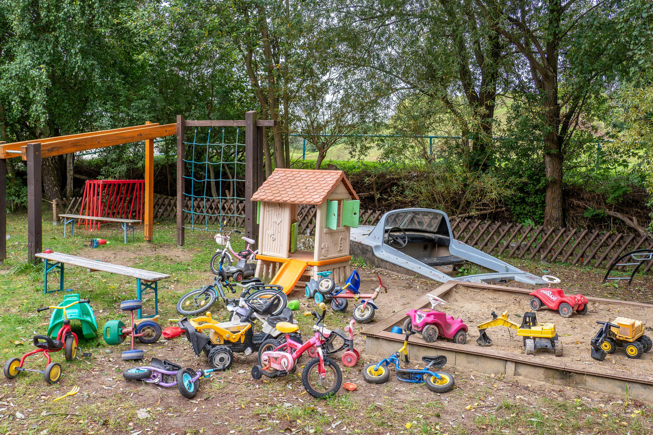 Spielplatz mit Spielhaus, Sandkasten, Dreirädern und Kinderrädern auf Gras.