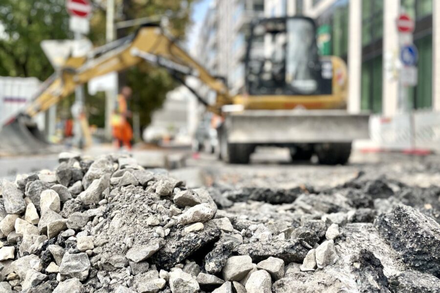 Steinhaufen im Vordergrund, Bagger und Person unscharf im Hintergrund.