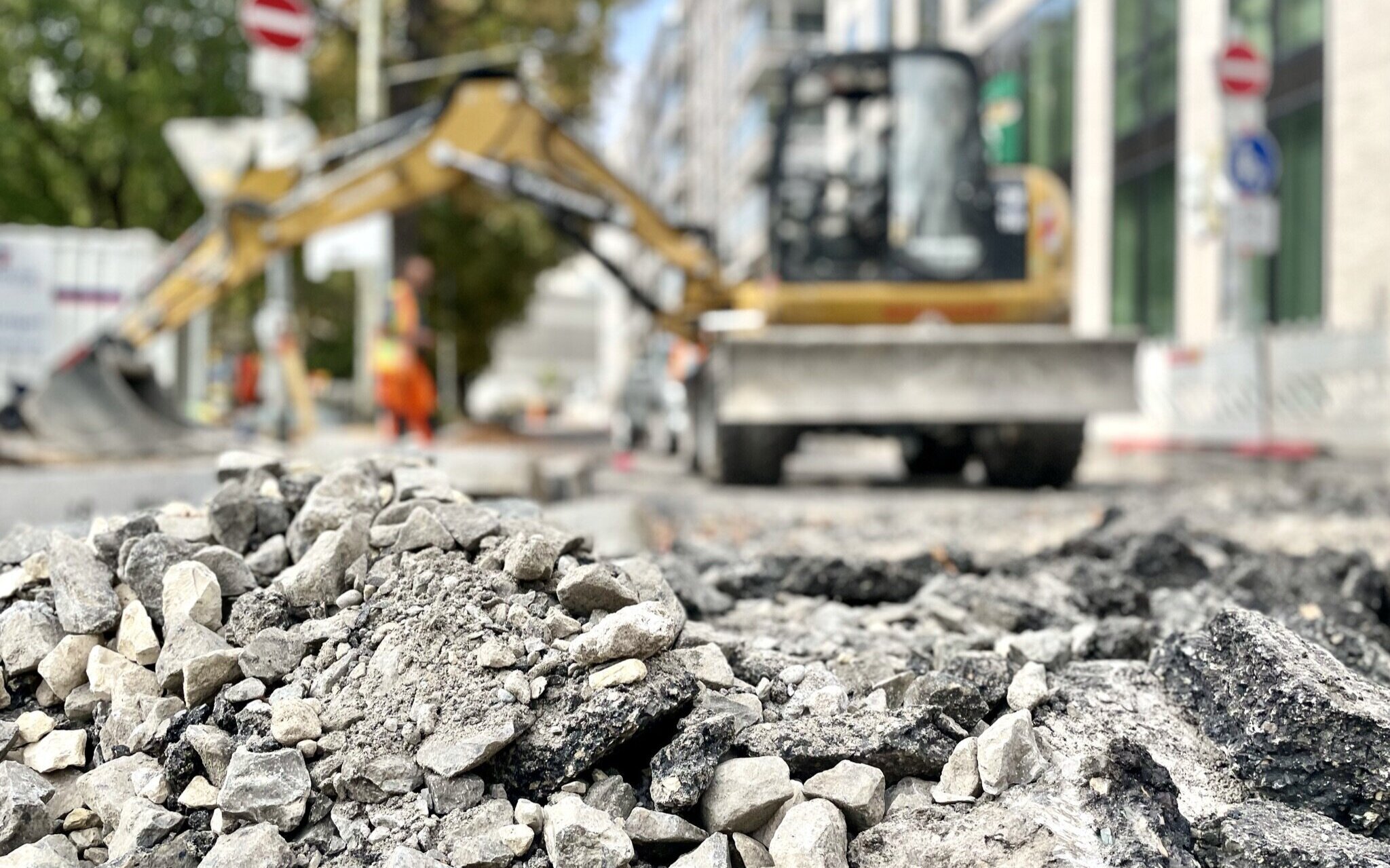 Steinhaufen im Vordergrund, Bagger und Person unscharf im Hintergrund.