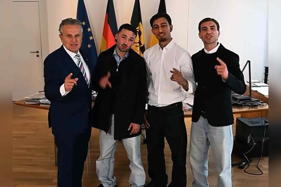 Vier Männer stehen lächelnd vor Flaggen in einem Raum mit Holzfußboden.