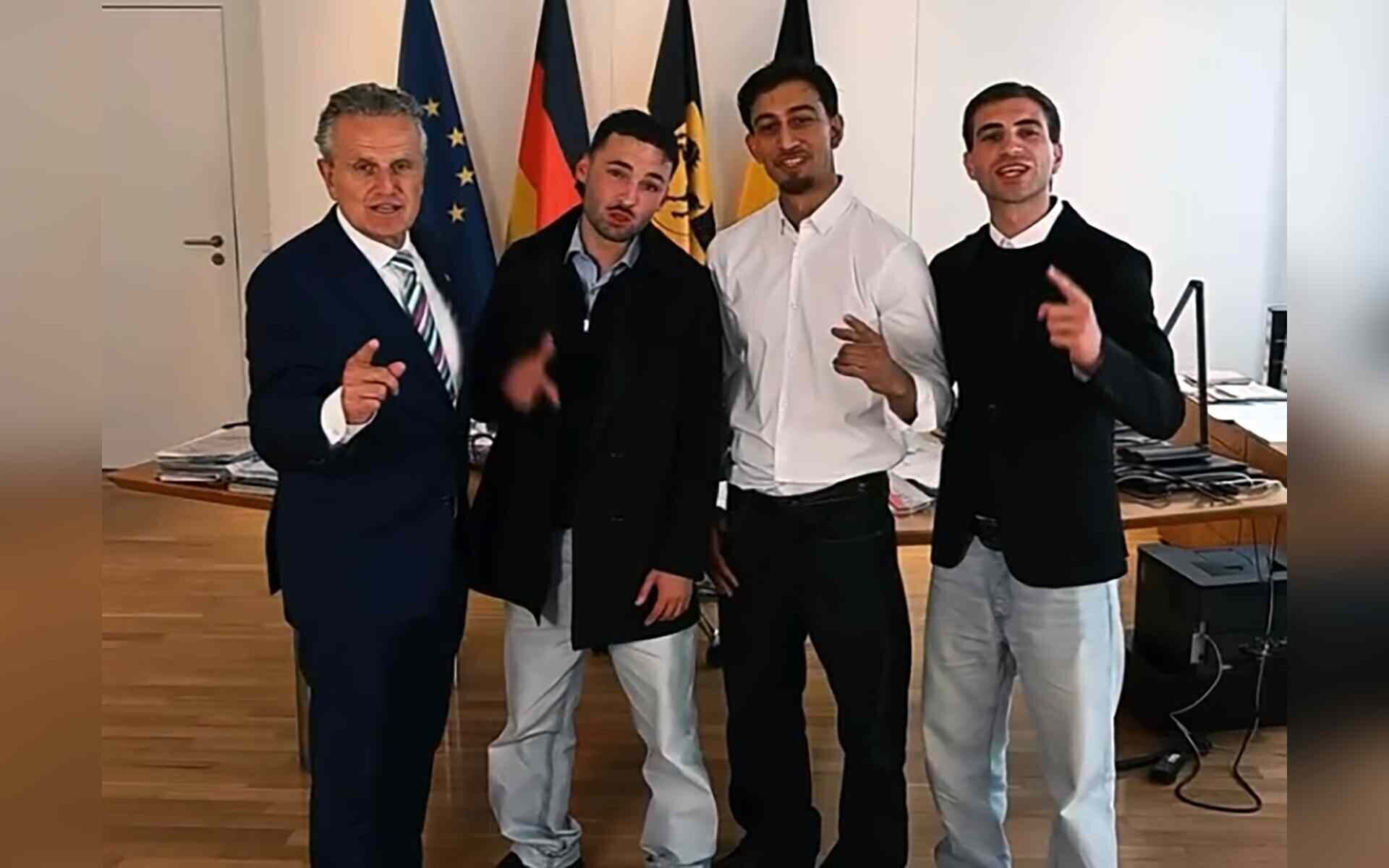 Vier Männer stehen lächelnd vor Flaggen in einem Raum mit Holzfußboden.