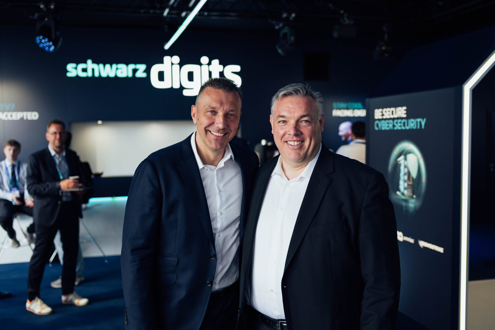 Zwei Männer in Anzügen lächeln, Hintergrund mit Schriftzug "schwarz digits".