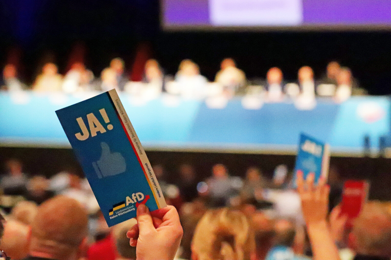 Person hält ein Schild mit "JA!" in einem Konferenzsaal.