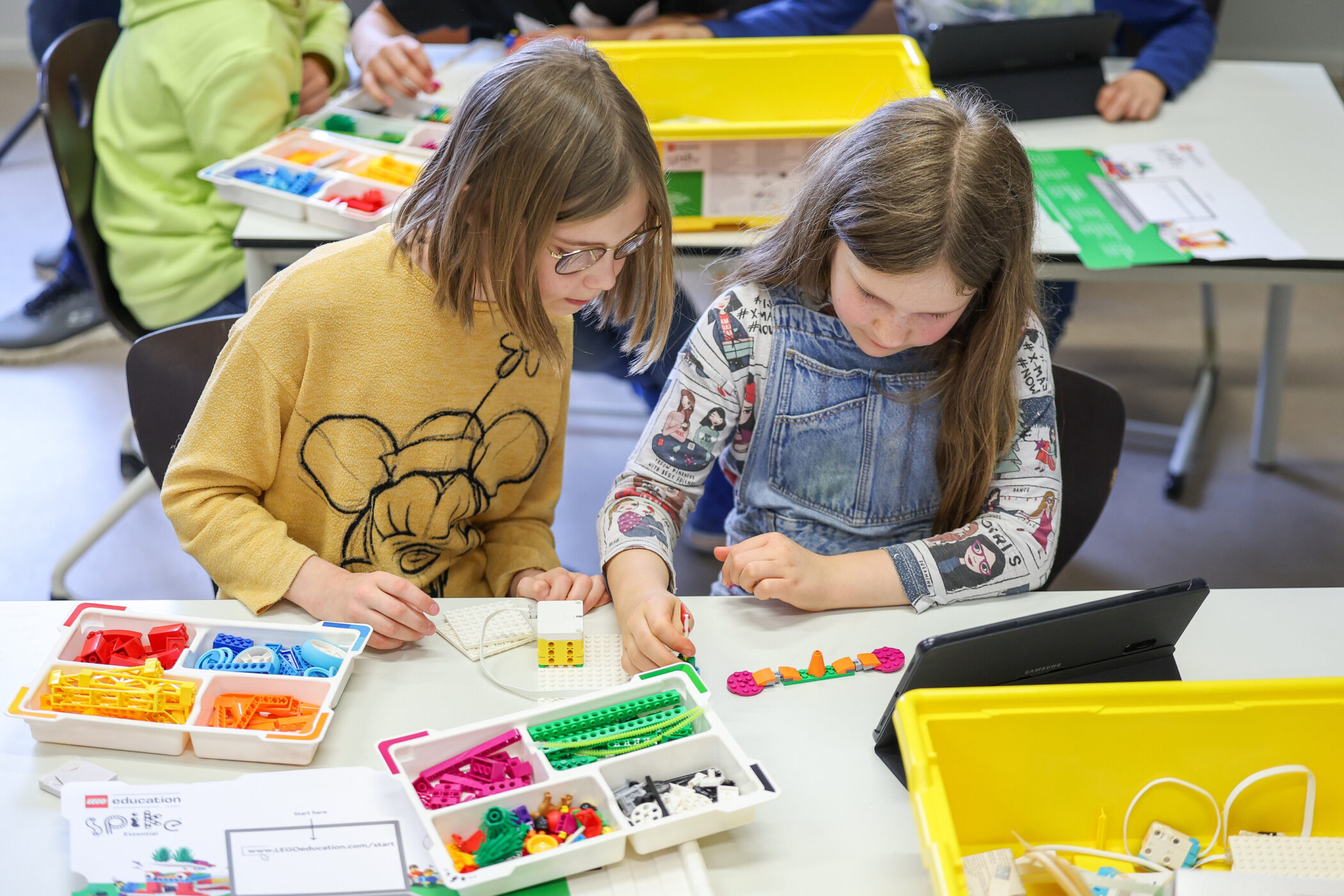 Zwei Kinder bauen mit LEGO-Steinen; bunter Bausatz auf dem Tisch.