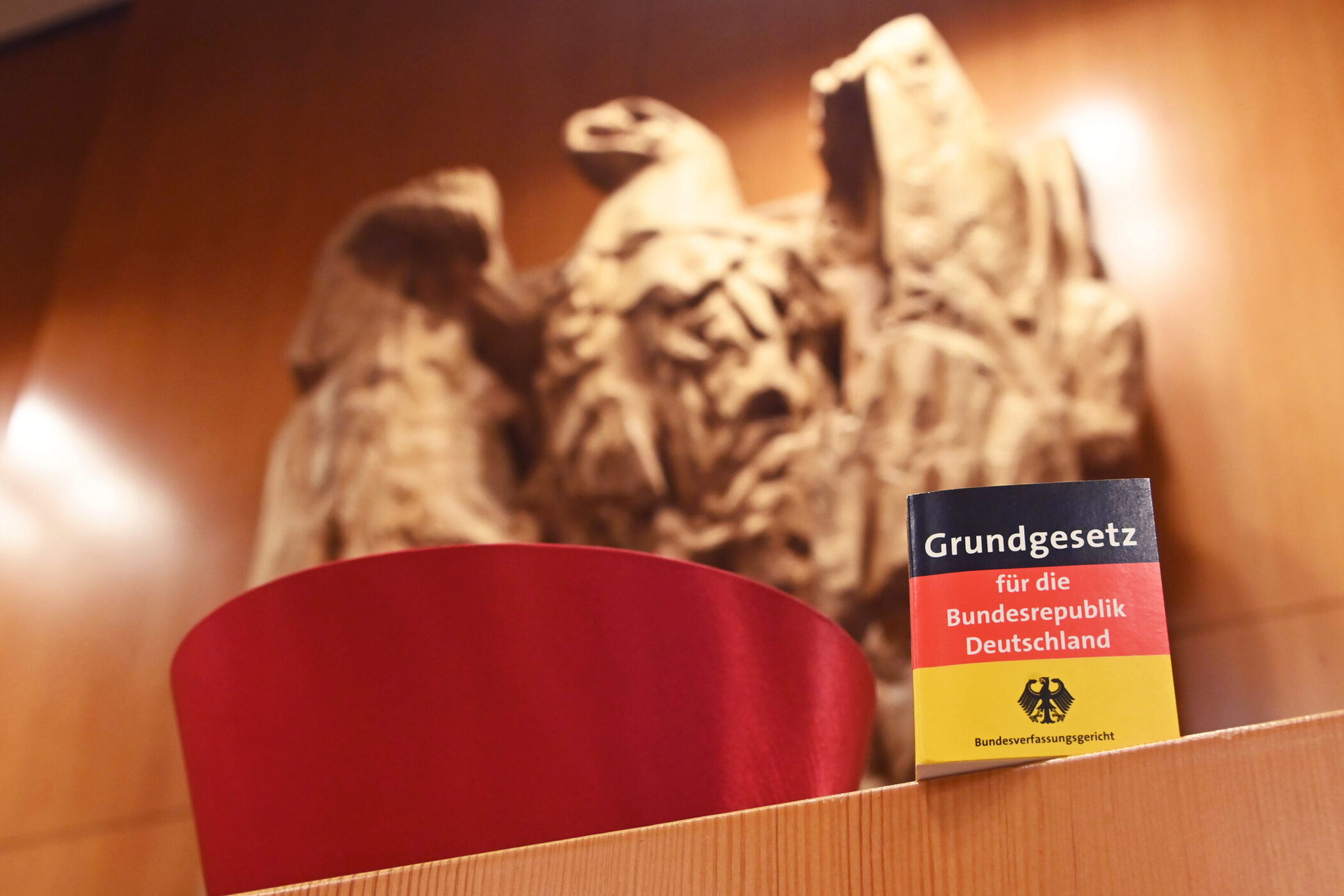 Grundgesetzbuch auf Holzplatte, im Hintergrund Adlerrelief an Holzwand.