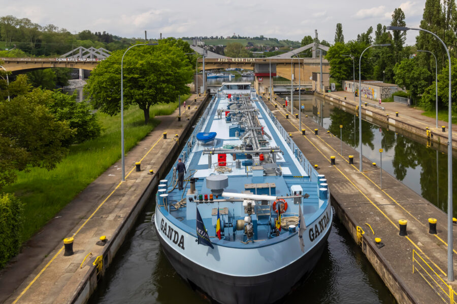 Großes Frachtschiff in Schleuse, Bäume, Brücke im Hintergrund. Schiffsschrift „GANDA“.