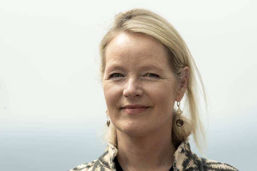 Person mit blonden Haaren und Ohrringen vor hellem Hintergrund.