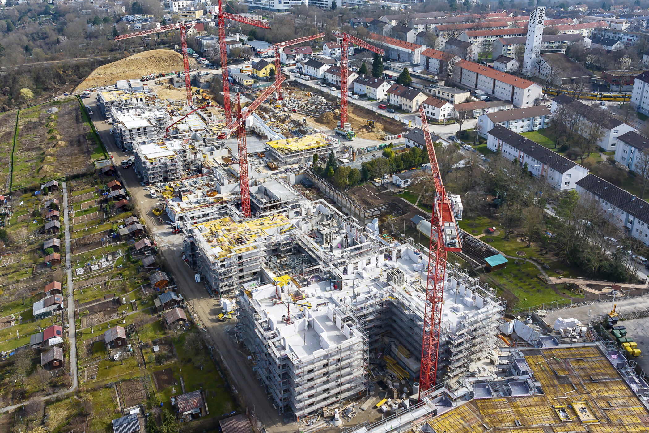 Luftaufnahme einer großen Baustelle mit mehreren Kränen und umliegender Wohnbebauung.