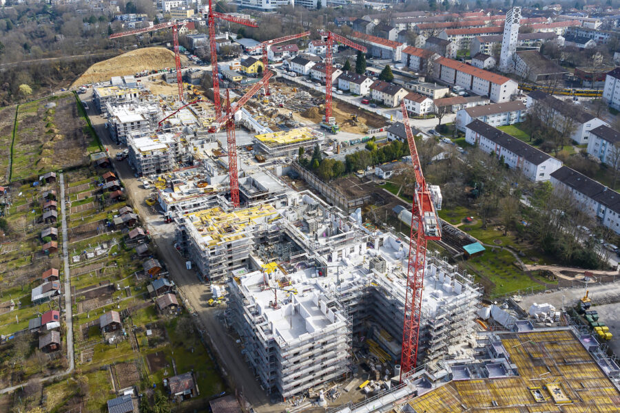 Luftaufnahme einer großen Baustelle mit mehreren Kränen und umliegender Wohnbebauung.