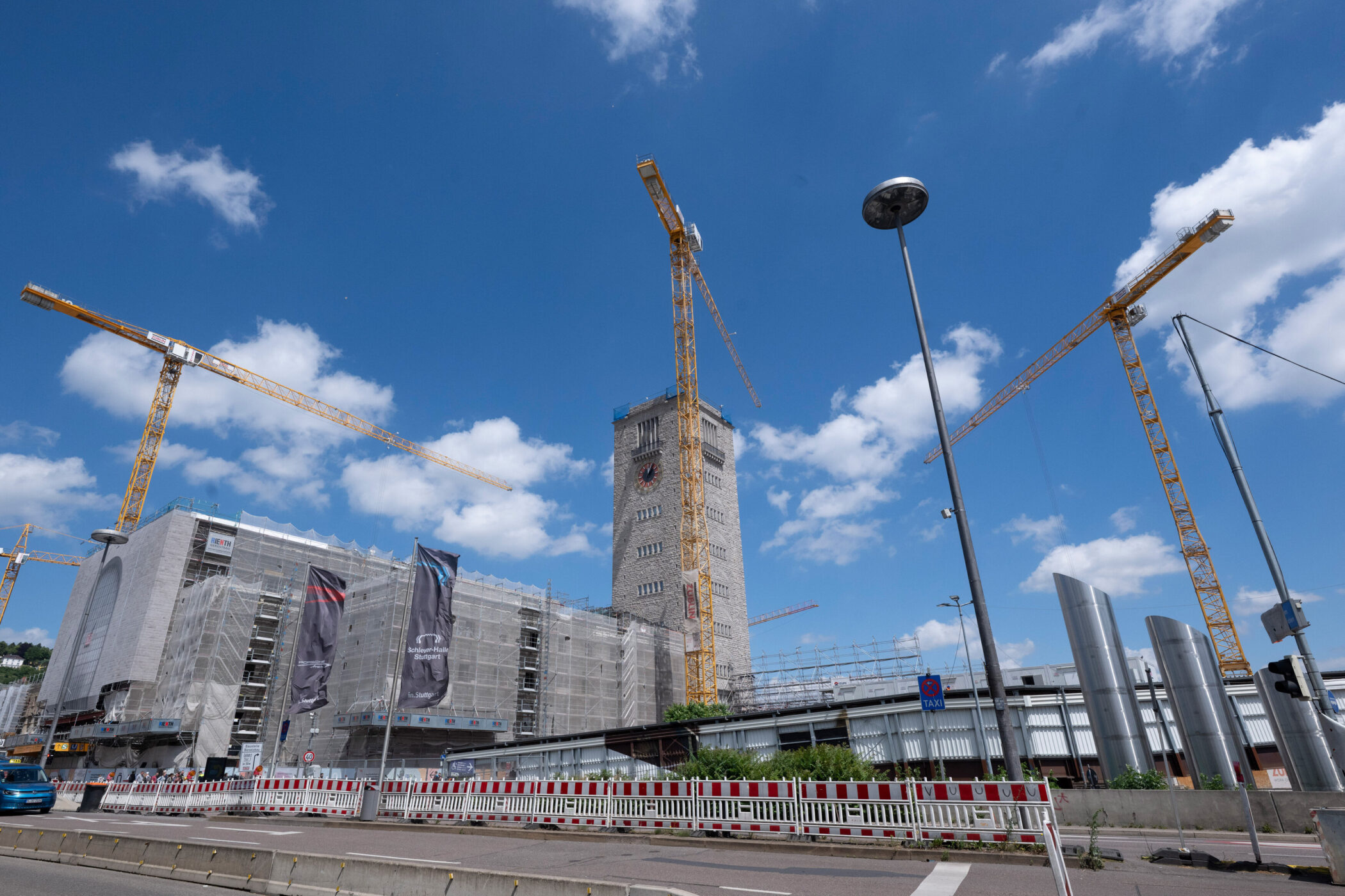 Kräne und Baugerüst an einem Turm bei blauem Himmel mit weißen Wolken.